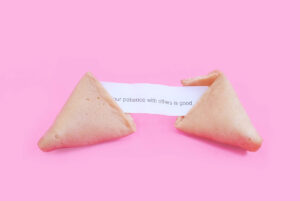 Geöffneter Glückskeks mit Spruch auf Papier, rosa Hintergrund