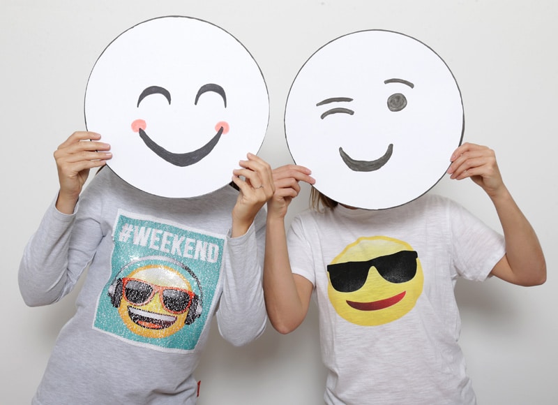 Zwei Menschen halten sich jeweils ein Emoji-Gesicht vors Gesicht.